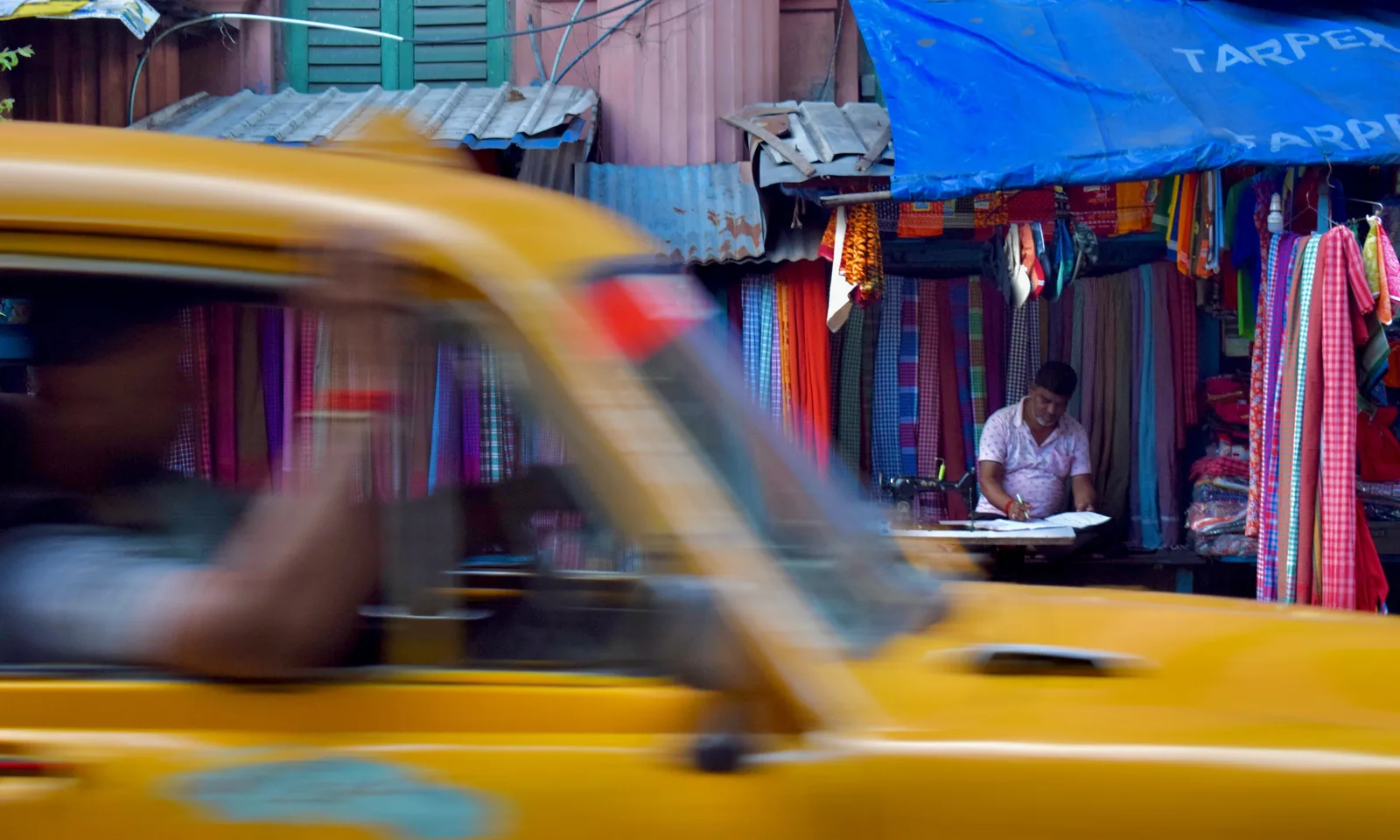 Yellow taxi in motion, tailor at work behind